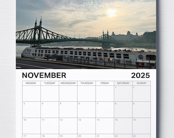 Könnte beinhalten: Ein November 2025 Kalender mit einem Foto einer Brücke über einen Fluss mit einem Boot im Vordergrund. Die Brücke ist grün und das Boot ist weiß. Der Himmel ist blau und es gibt Wolken am Himmel.