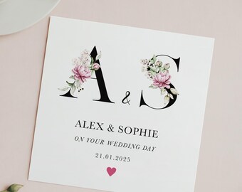 May include: A wedding card with the letters A and S decorated with pink and white flowers. The text reads "Alex & Sophie On Your Wedding Day 21.01.2025" with a small pink heart.