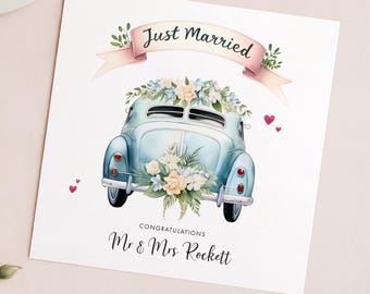 May include: A light blue vintage car decorated with white flowers and a pink ribbon banner that says "Just Married". The car is driving away with two red hearts in the air. The text "Congratulations Mr & Mrs Rockett" is below the car.