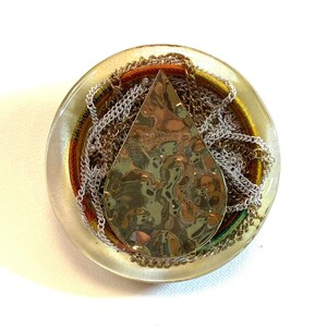 May include: A clear resin pendant featuring a gold teardrop-shaped charm and a variety of colourful and metallic chains inside.