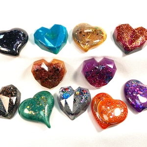 May include: Ten heart-shaped resin ornaments with glitter embedded in the resin. The hearts are in various colours, including black, teal, gold, orange, red, purple, green, and grey.