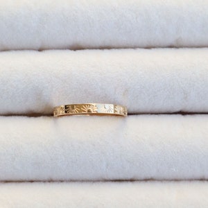 May include: A gold band ring with a sunburst design. The ring is on a white background.