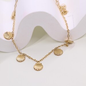 Peut inclure: Un collier en chaîne dorée avec cinq petits pendentifs en forme de coquillage dorés.
