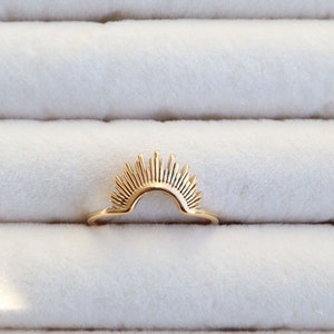 May include: A gold ring featuring a sunburst design. The ring is crafted from metal and has a smooth finish.