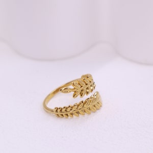 May include: A gold ring featuring a leaf design. The ring is open on one side and has a delicate, intricate design.