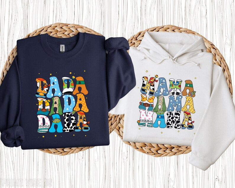 May include: A navy blue crew neck sweatshirt and a white hooded sweatshirt. Both sweatshirts feature colourful text designs. The navy sweatshirt says "DADA" in a stacked design. The white sweatshirt says "MAMA" in a stacked design.