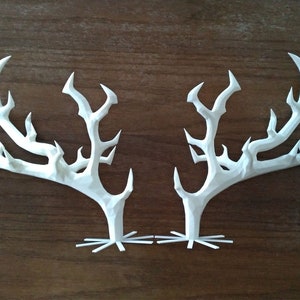 Könnte beinhalten: Zwei weiße Papier-Hirschgeweihe mit filigranen Details. Die Geweihe sind symmetrisch und haben ein zartes, fast skelettartiges Aussehen.