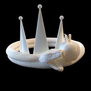 Può includere: Una corona bianca stampata in 3D con tre punte, un serpente avvolto attorno alla base e una mela nella bocca del serpente.