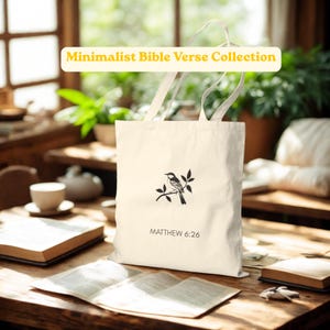May include: A cream-colored canvas tote bag featuring a black line drawing of a small bird perched on a branch. Below the bird, the text reads "MATTHEW 6:26". The bag has two matching fabric handles and is displayed in a vertical orientation.