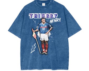 May include: A blue denim t-shirt with a faded, vintage look. The shirt features a graphic print of soccer player Thierry Henry wearing a blue and white jersey with the number 12. The text "Thierry Henry" is printed in purple above the image.