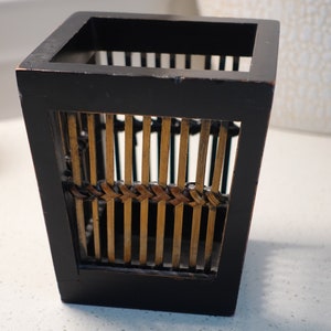 Puede incluir: Un porta lápices de madera negro de forma cuadrada con un inserto de bambú tejido.