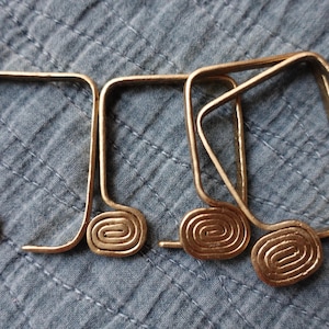May include: Five gold-toned metal curtain tiebacks with a spiral design. The tiebacks are in the shape of a rectangle with rounded corners.