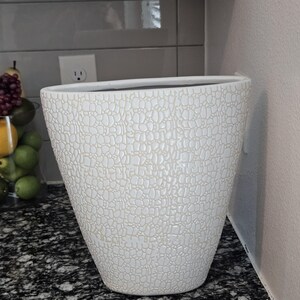 May include: White ceramic planter with a textured, pebble-like pattern. The tall, oval-shaped pot has a wide opening and a slightly tapered base. The planter is set against a neutral background.