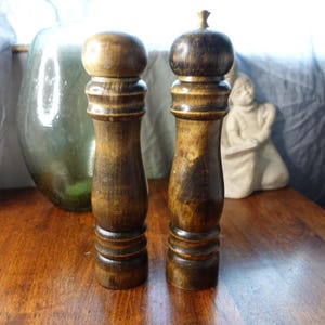 Może przedstawiać: Zestaw dwóch drewnianych solniczek i pieprzniczek z ciemnobrązowym wykończeniem drewna. Solniczki mają klasyczny design z okrągłym wierzchołkiem i cylindrycznym korpusem.