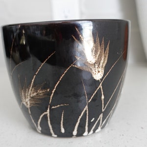 May include: A black ceramic planter with a white and brown floral design. The planter has a rounded shape and a smooth finish.