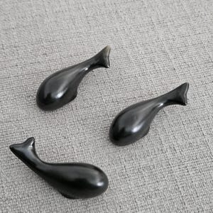 May include: Three smooth, black, whale-shaped chopstick rests with a glossy finish. Each piece features a rounded body, a tapered tail, and a curved silhouette, designed to hold utensils securely while resting on a flat surface.