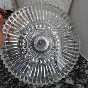 May include: Clear glass serving dish with three divided sections and a central circular area. The dish has a ribbed design radiating from the centre and a scalloped edge. Suitable for serving appetizers or snacks.