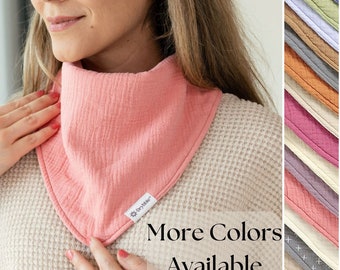 Puede incluir: Un babero para bebé de color coral con una superficie texturizada. El babero es triangular y tiene un escote redondeado. Las palabras "More Colors Available" se muestran debajo, con una carta de colores de baberos en varios colores a la derecha.