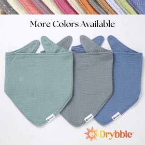 May include: Three triangular baby bibs in different shades of blue. The bibs are made of soft, absorbent fabric and have a snap closure. The bibs are labeled "Drybbble".