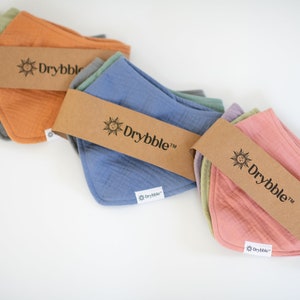 Puede incluir: Tres juegos de baberos para bebés multicolores con una etiqueta de papel marrón que dice "Drybbble" con un gráfico de sol.
