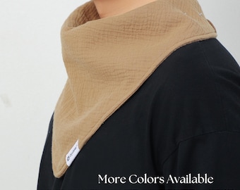 Puede incluir: Babero triangular beige de tela texturizada. El babero está alrededor del cuello de una persona que lleva una camisa negra. El texto "More Colors Available" está en la parte inferior de la imagen.