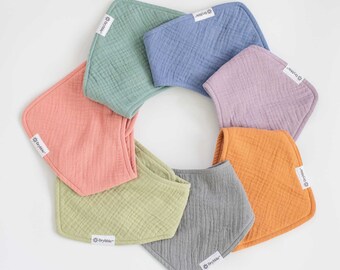 May include: A collection of soft, pastel-colored baby bibs arranged in a circular pattern. The bibs are in shades of pink, green, blue, purple, orange, and gray. Each bib has a tag with the brand name "Drybibble".