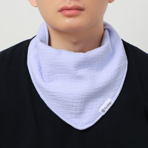 May include: A light blue, triangular baby bib made of a soft, textured fabric. The bib is worn around the neck and has a small white tag with the brand name "Drybibble". The bib is designed to catch spills and drool.