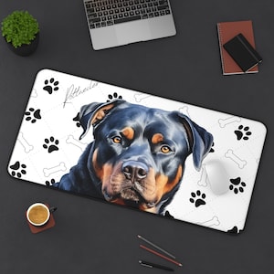 May include: A rectangular desk mat featuring a Rottweiler dog portrait with a black and tan coat. The white mat has a paw print and bone pattern, with the word "Rottweiler" in script. A computer mouse rests on the mat.