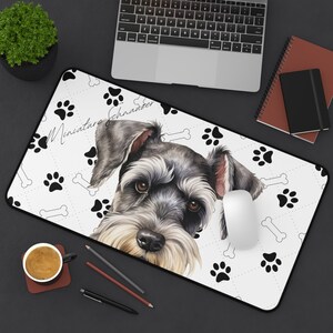 Op de afbeelding: Een rechthoekige muismat met een portret van een Dwergschnauzer hond. De mat heeft een witte achtergrond met zwarte pootafdrukken en botillustraties. Het portret van de hond staat in het midden, met de woorden "Miniature Schnauzer" in script.