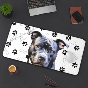 May include: A rectangular desk mat featuring a detailed illustration of a Staffordshire Bull Terrier with a black and white color scheme. The mat has a white background with black paw prints and bone patterns. The text "Staffordshire Bull Terrier" is printed on the mat.
