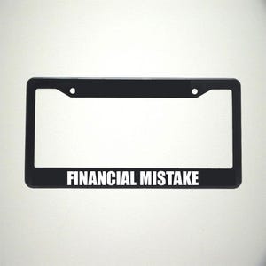 May include: Black plastic license plate frame with the text "FINANCIAL MISTAKE" in white letters.