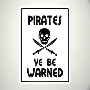Könnte beinhalten: Ein weißes Schild mit schwarzem Text und einer Grafik mit Totenkopf und Knochen. Das Schild lautet "Pirates Ye Be Warned".