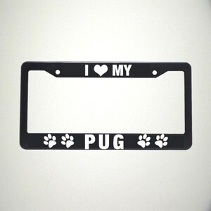 May include: Black metal license plate frame with white text that reads "I love my PUG" with paw prints on either side of the word PUG.