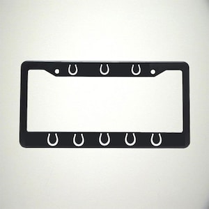May include: Black license plate frame with white horseshoe designs.