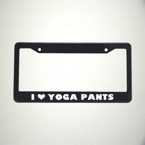 May include: Black plastic license plate frame with white text that reads "I ♥ YOGA PANTS".