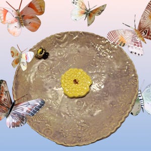 May include: A decorative, round, bronze-colored plate with an embossed floral design. A yellow, flower-shaped object sits in the center. Several colorful butterfly illustrations are arranged around the plate, creating a whimsical, nature-inspired theme.