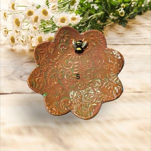 May include: A small, scalloped ceramic dish with a green and orange floral pattern. A small bee figurine is attached to the dish.