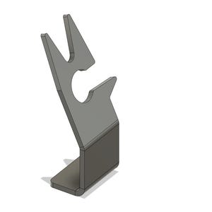 Puede incluir: Un soporte para teléfono de metal gris con un diseño único. El soporte tiene una base rectangular y un soporte en ángulo con un recorte curvo y dos púas en la parte superior. El soporte está diseñado para sostener un teléfono.