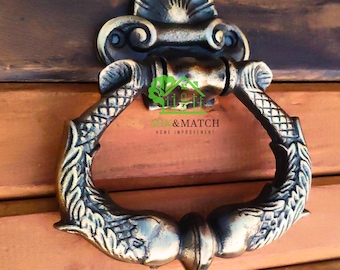 Könnte beinhalten: Verzierter Türklopfer aus Bronze mit Fischmotiv. Der Türklopfer hat eine dekorative Rückplatte und einen ringförmigen Griff. Der Text "XIM & MATCH HOME IMPROVEMENT" ist sichtbar.