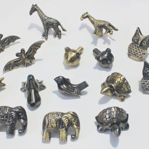 May include: A selection of metal animal figurines, featuring giraffes, bats, bears, birds, deer, elephants, turtles, and owls. The figurines have detailed textures and come in various metallic finishes. These small sculptures are suitable for home decoration.