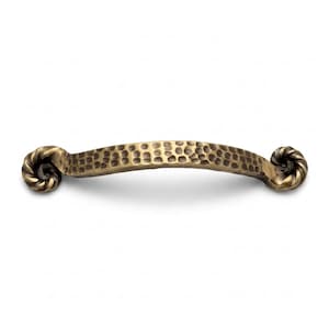 May include: A curved cabinet handle with a dark brass finish and a hammered, dimpled texture across the center. The ends of the handle feature a decorative, spiraled rope-like design that curls inward, providing a distinct contrast to the center.
