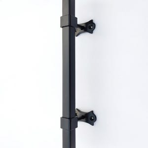 May include: A black, rectangular door pull with a square top and bottom. The pull is mounted on a white wall with two decorative brackets. The door pull is approximately 12 inches in length.