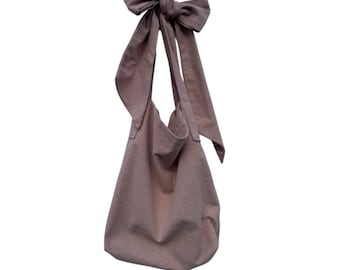 May include: A dusty rose-coloured tote bag with a large bow at the top. The bag is made of a soft, textured fabric.