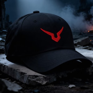 May include: Black baseball cap with a red emblem on the front. The cap is sitting on a concrete surface, with a night sky background, a full moon, and a spotlight shining on the cap. The background also includes a fire and rubble.