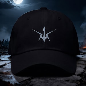 May include: Black baseball cap with a white embroidered emblem. The cap features a curved brim and a structured crown. The emblem is a stylized, symmetrical design. The background shows a full moon in a dark, cloudy sky.