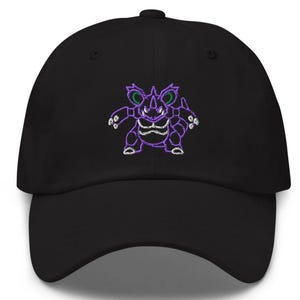 May include: Black baseball cap with a purple embroidered design of a cartoon creature. The creature has green accents and white details. The cap has a curved brim and an adjustable strap.