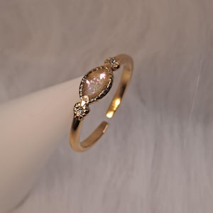 May include: A gold ring with a clear oval-shaped stone and two smaller clear stones on the band.
