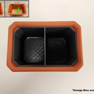 May include: A terracotta planter with a black divider inside, creating two compartments. The planter is empty and the orange bins are not included.