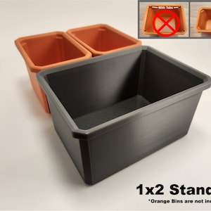 May include: A grey plastic storage bin with a 1x2 standard label. The bin is empty, but two orange plastic bins are visible in the background. The orange bins are not included.