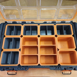 May include: A black and orange plastic storage box with multiple compartments. The box has a clear lid and is open, revealing the compartments inside.